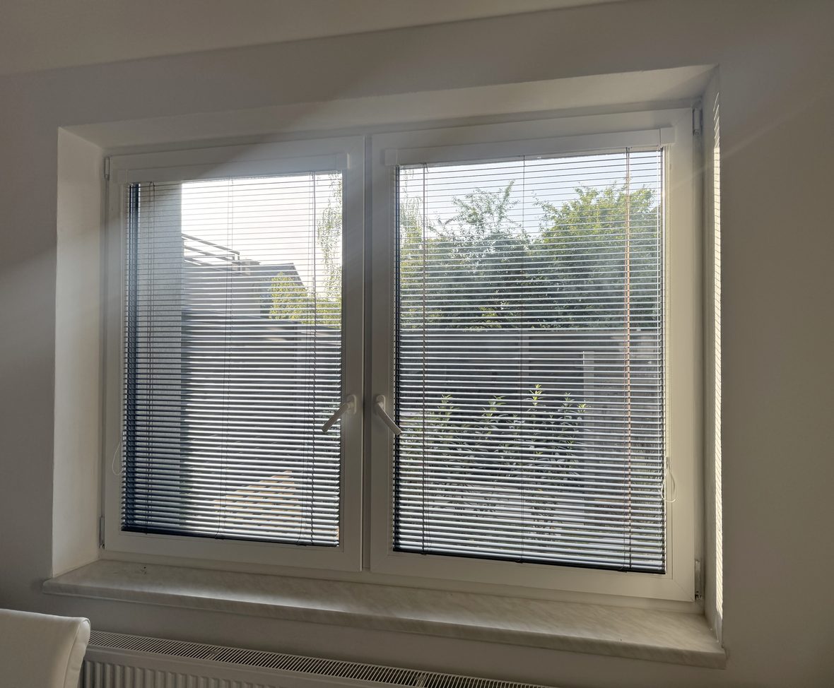 Vnitřní horizontální žaluzie s naklopenými lamelami v okně obývacího pokoje